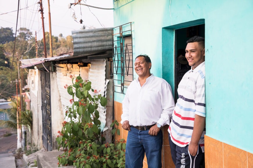 Salvadoran Father and Son standing in front of home smiling.