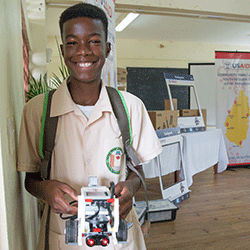 A boy from Saint Lucia smiles while holding a Lego robot.
