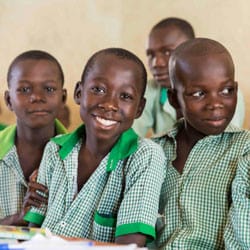 Four Nigerian boys in their classroom wearing green and white checkered uniforms and smiling.