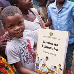 A boy in Mozambique smiles and hold a book written in his local language.