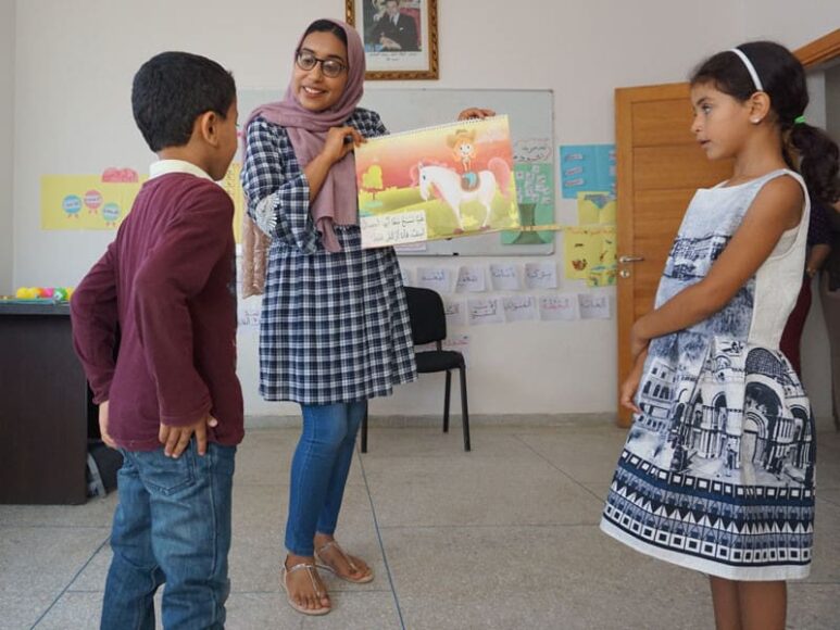 A Moroccan teacher looks at a book with a young boy and girl.