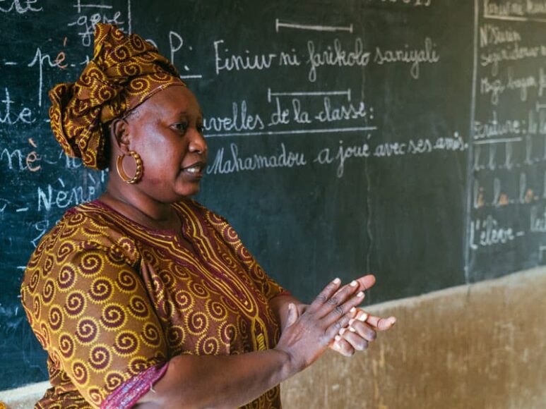 A teacher stands in front of a chalkboard in Mali.